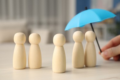 Photo of Woman holding umbrella over human figures at white wooden table indoors, closeup. Insurance concept