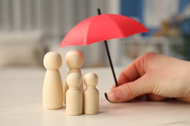 Photo of Woman holding umbrella over human figures at white wooden table indoors, closeup. Insurance concept