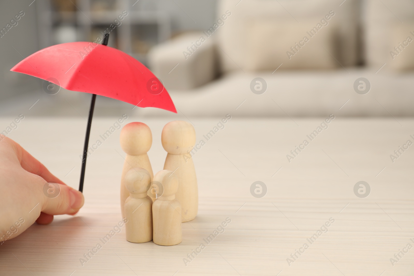 Photo of Insurance concept. Woman holding umbrella over human figures at white wooden table indoors, closeup. Space for text