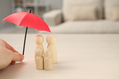 Photo of Insurance concept. Woman holding umbrella over human figures at white wooden table indoors, closeup. Space for text