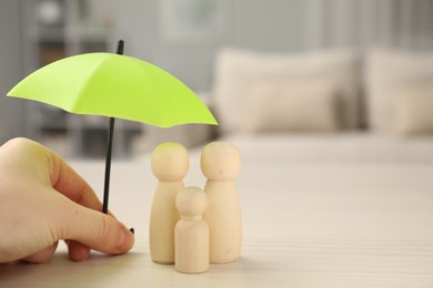 Photo of Insurance concept. Woman holding umbrella over human figures at white wooden table indoors, closeup. Space for text