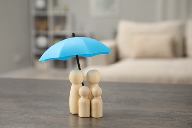 Photo of Human figures under umbrella on grey table indoors. Insurance concept