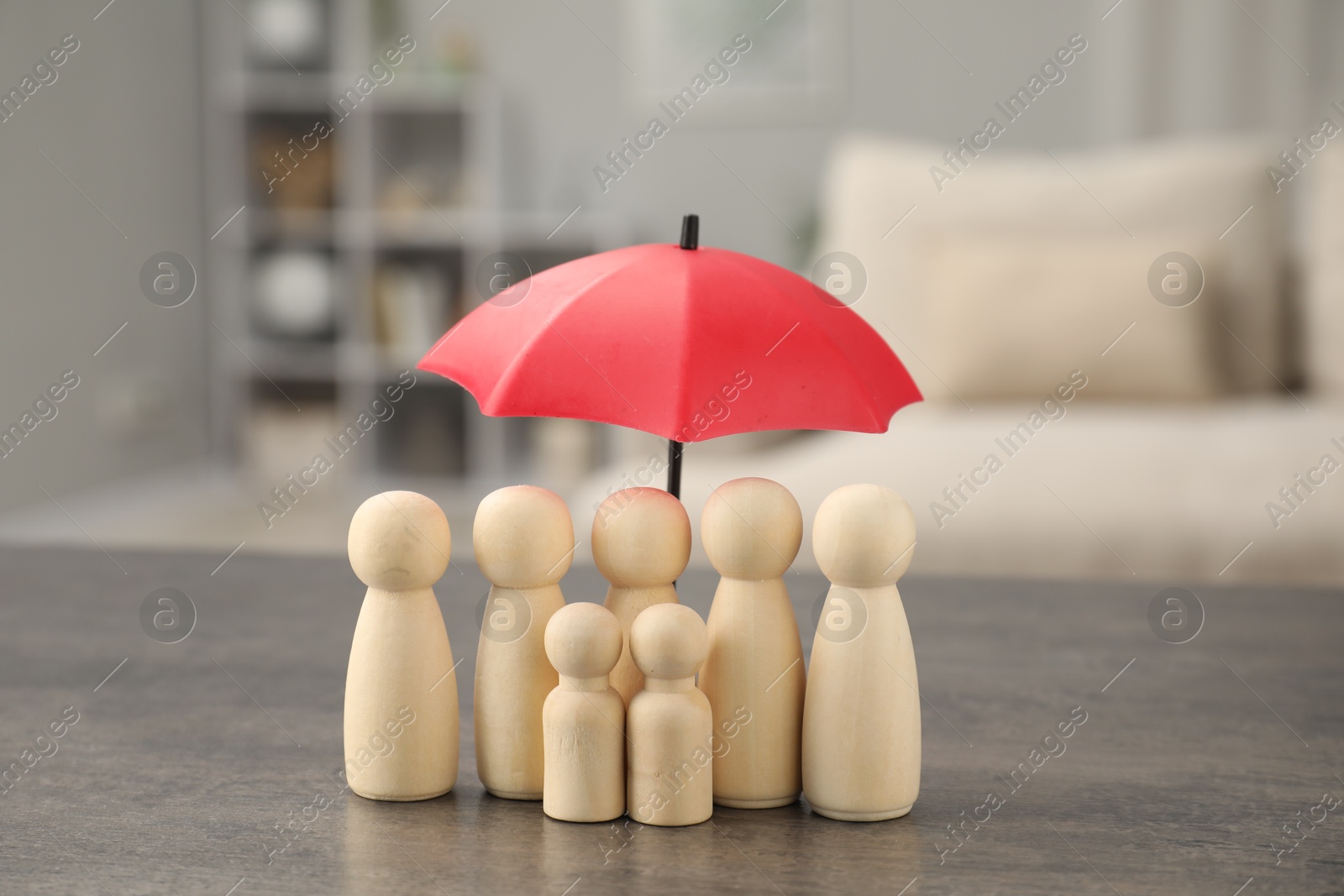 Photo of Human figures under umbrella on grey table indoors. Insurance concept