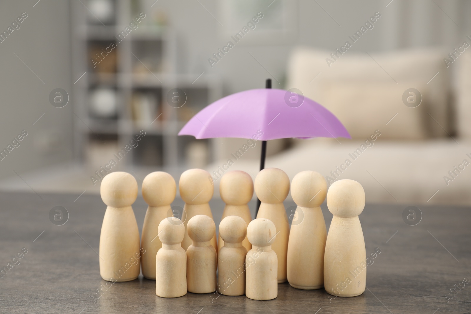 Photo of Human figures under umbrella on grey table indoors. Insurance concept