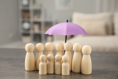 Photo of Human figures under umbrella on grey table indoors. Insurance concept