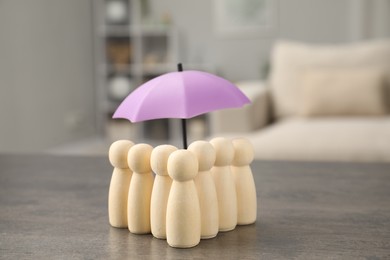 Photo of Human figures under umbrella on grey table indoors. Insurance concept