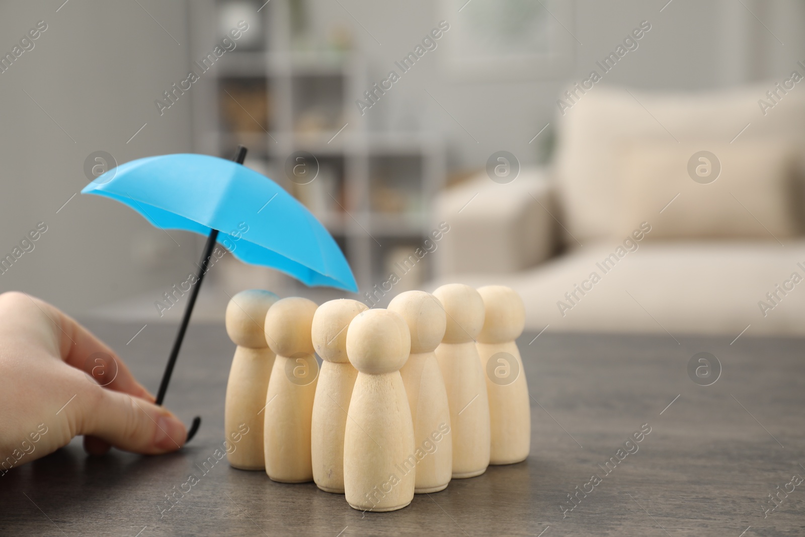 Photo of Woman holding umbrella over human figures at grey table indoors, closeup. Insurance concept