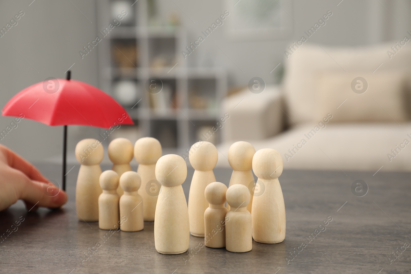 Photo of Woman holding umbrella over human figures at grey table indoors, closeup. Insurance concept