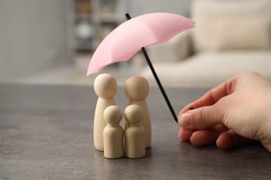 Photo of Woman holding umbrella over human figures at grey table indoors, closeup. Insurance concept