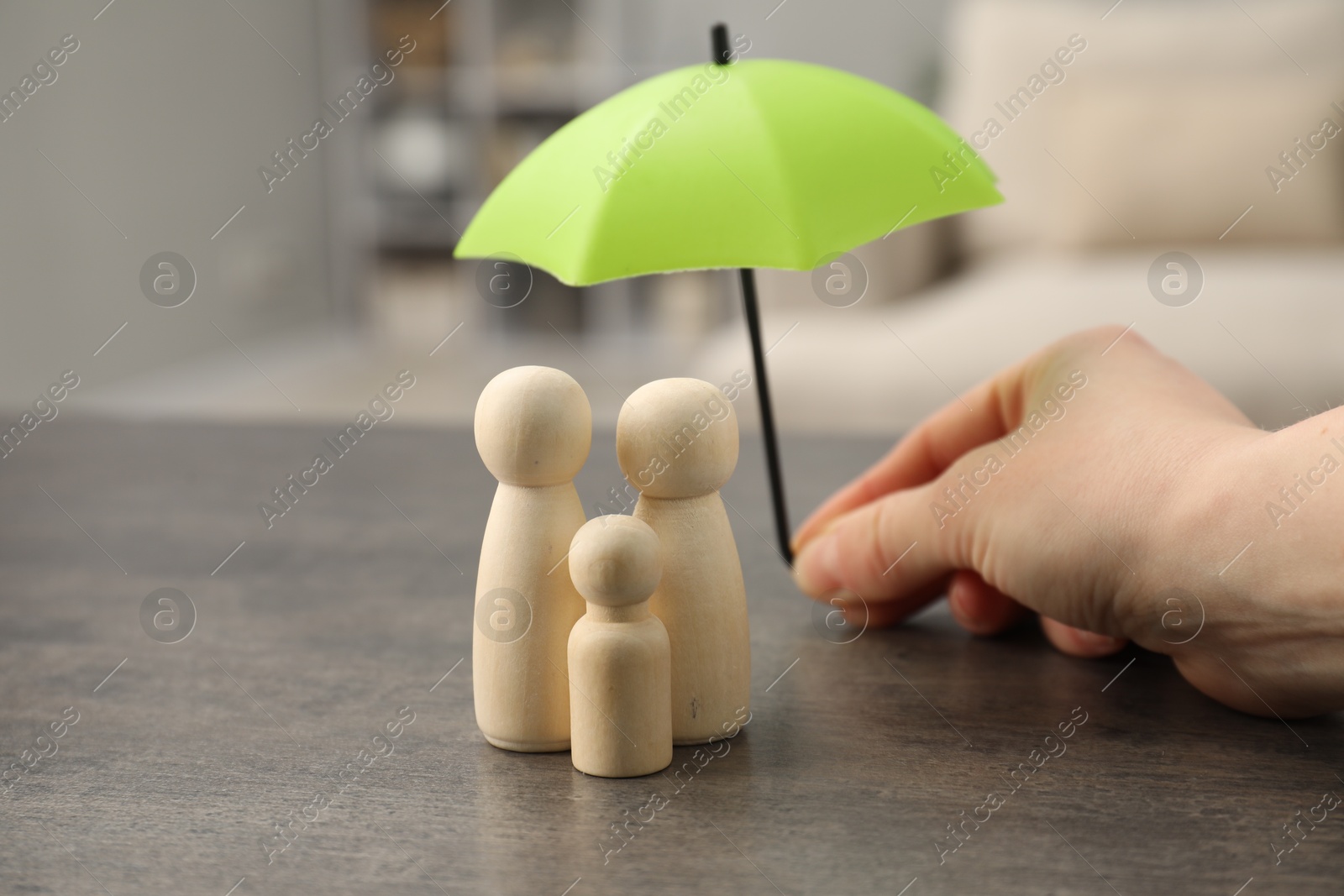 Photo of Woman holding umbrella over human figures at grey table indoors, closeup. Insurance concept