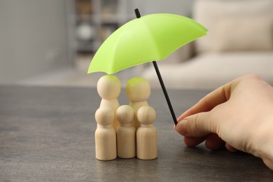 Photo of Woman holding umbrella over human figures at grey table indoors, closeup. Insurance concept