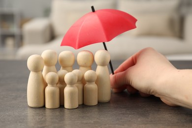 Photo of Woman holding umbrella over human figures at grey table indoors, closeup. Insurance concept