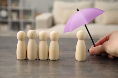 Photo of Woman holding umbrella over human figures at grey table indoors, closeup. Insurance concept