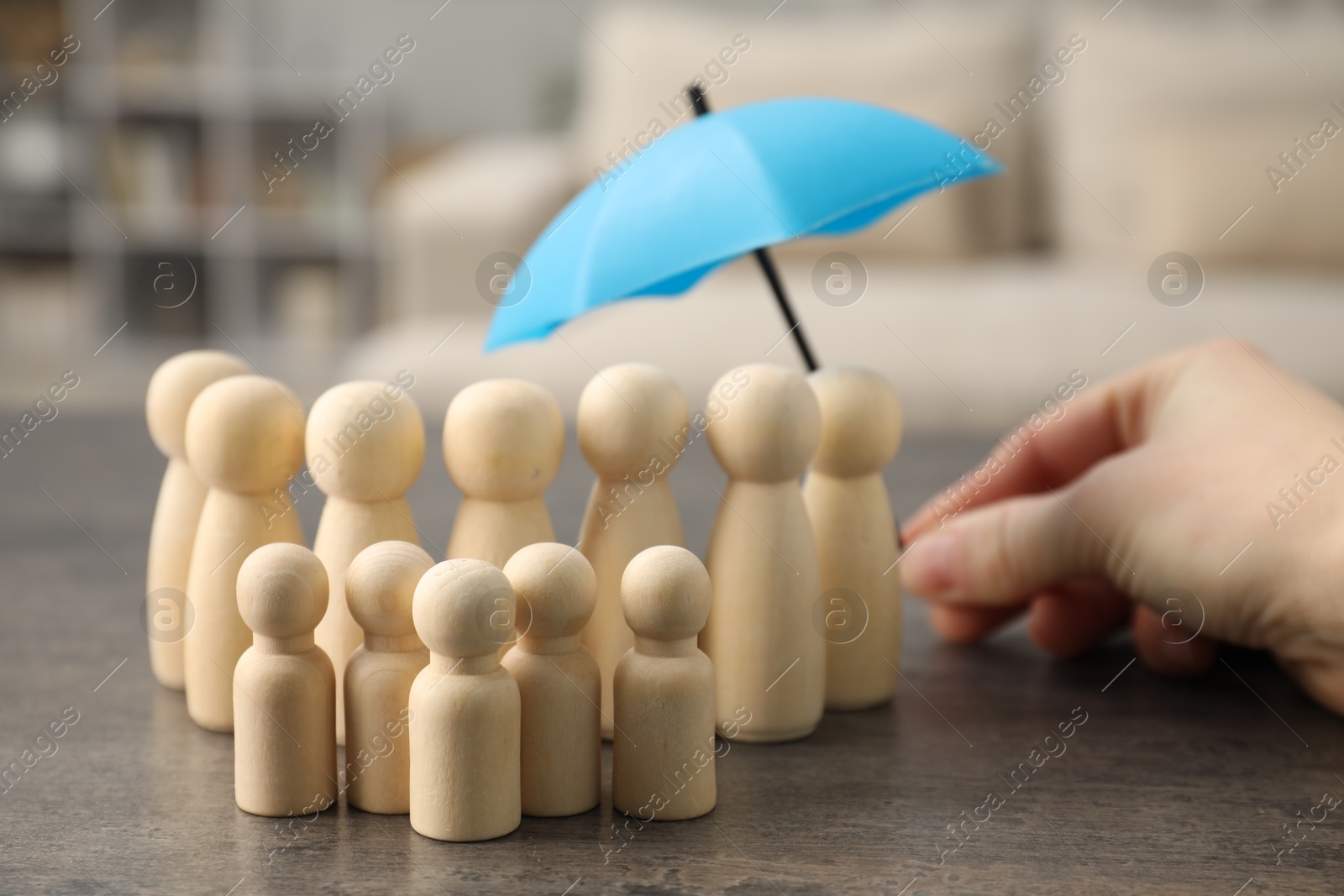 Photo of Woman holding umbrella over human figures at grey table indoors, closeup. Insurance concept