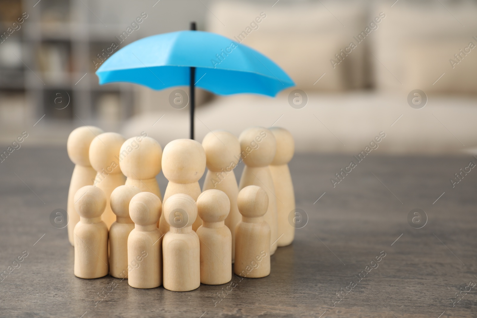 Photo of Human figures under umbrella on grey table indoors, space for text. Insurance concept