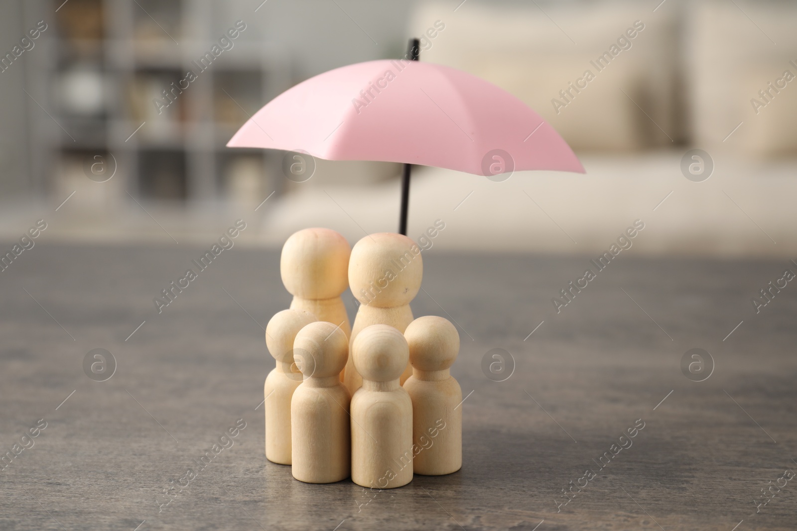 Photo of Human figures under umbrella on grey table indoors. Insurance concept