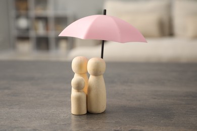 Photo of Human figures under umbrella on grey table indoors. Insurance concept