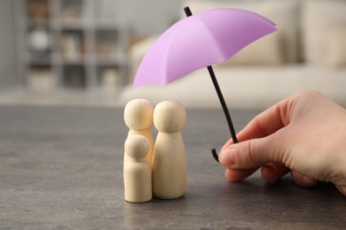 Photo of Woman holding umbrella over human figures at grey table indoors, closeup. Insurance concept