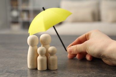 Photo of Woman holding umbrella over human figures at grey table indoors, closeup. Insurance concept