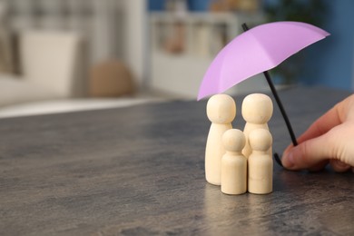 Photo of Insurance concept. Woman holding umbrella over human figures at grey table indoors, closeup. Space for text