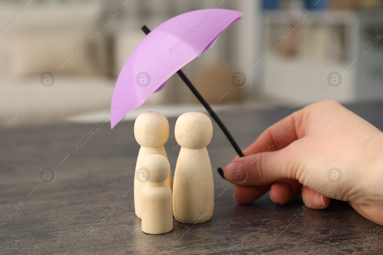 Photo of Woman holding umbrella over human figures at grey table indoors, closeup. Insurance concept