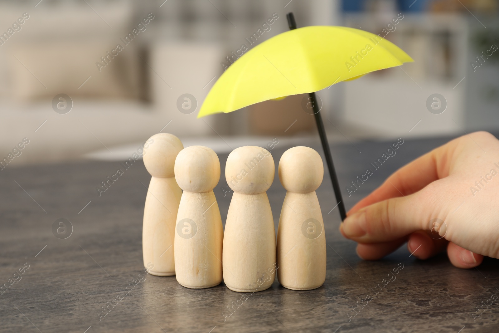 Photo of Woman holding umbrella over human figures at grey table indoors, closeup. Insurance concept