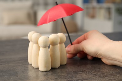 Photo of Woman holding umbrella over human figures at grey table indoors, closeup. Insurance concept