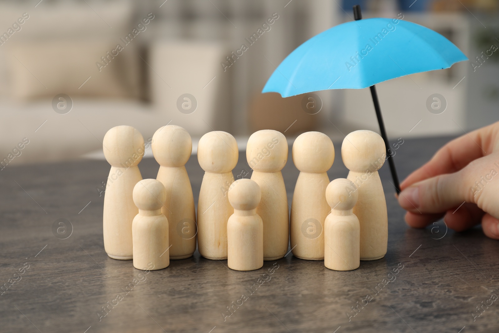 Photo of Woman holding umbrella over human figures at grey table indoors, closeup. Insurance concept