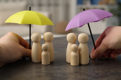 Photo of Woman holding umbrellas over human figures at grey table indoors, closeup. Insurance concept