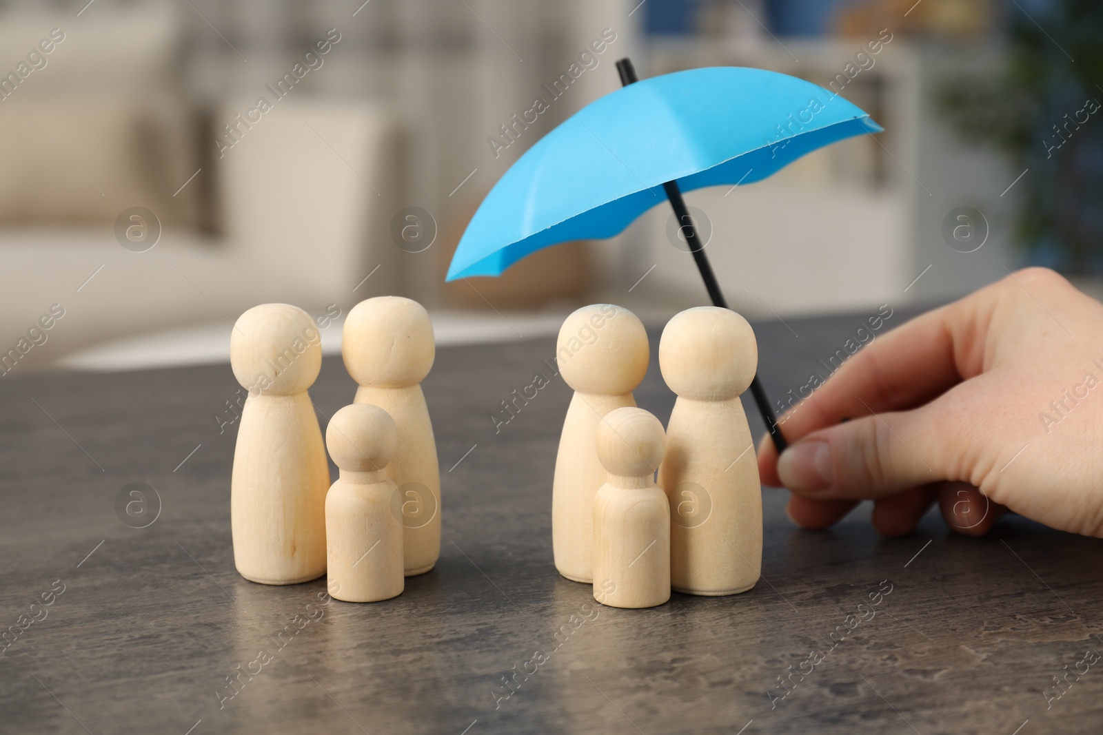 Photo of Woman holding umbrella over human figures at grey table indoors, closeup. Insurance concept