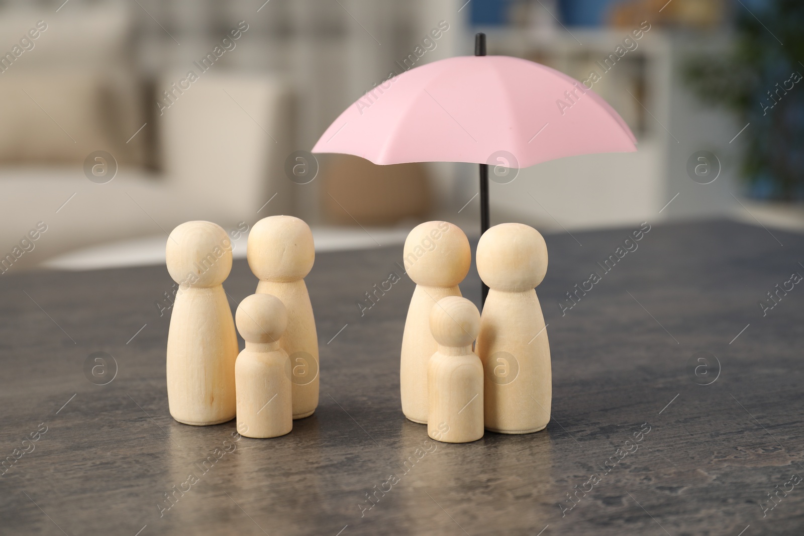 Photo of Human figures under umbrella and wooden ones on grey table indoors. Insurance concept