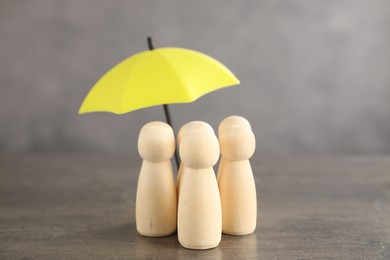 Photo of Human figures under umbrella on grey table. Insurance concept