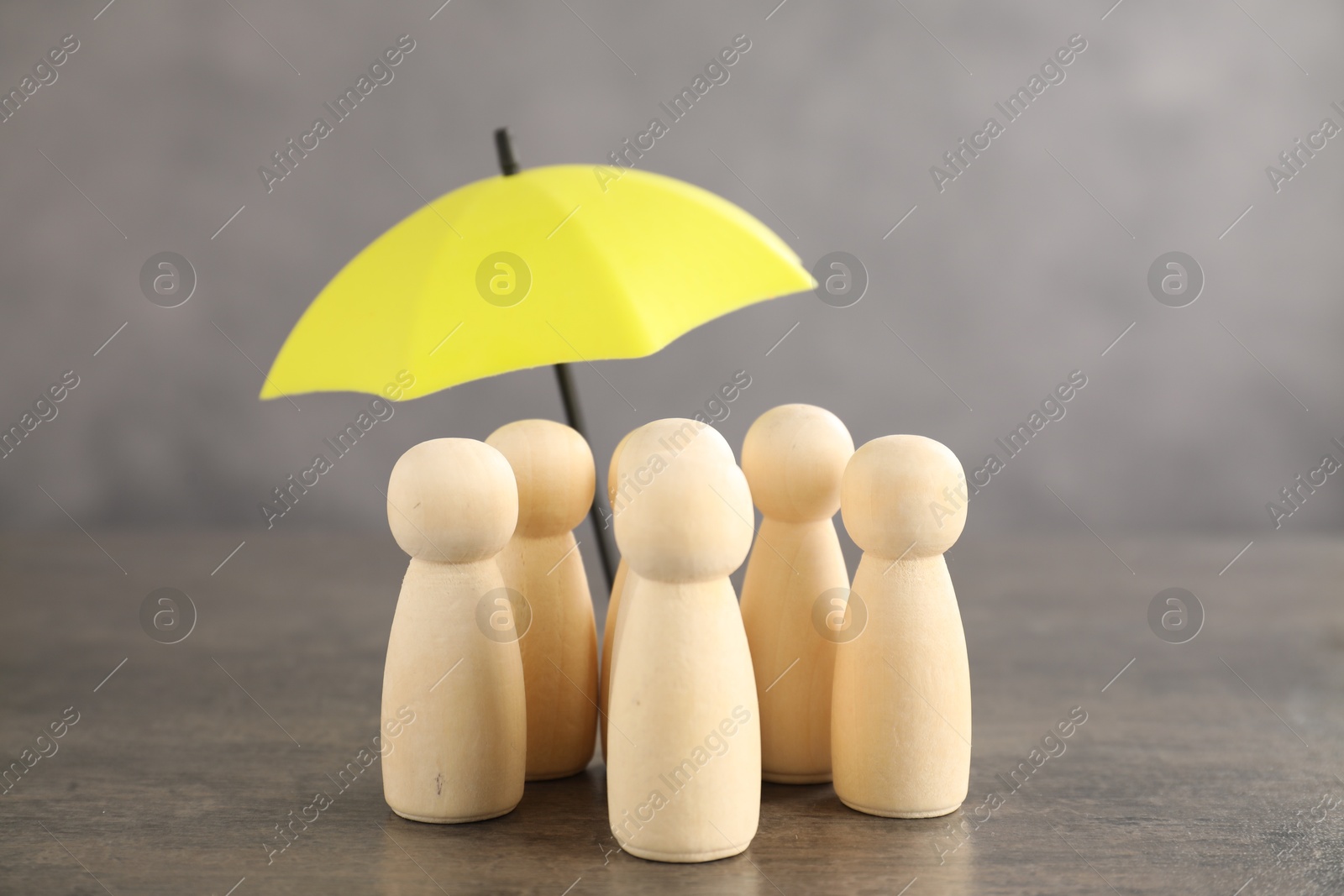 Photo of Human figures under umbrella on grey table. Insurance concept