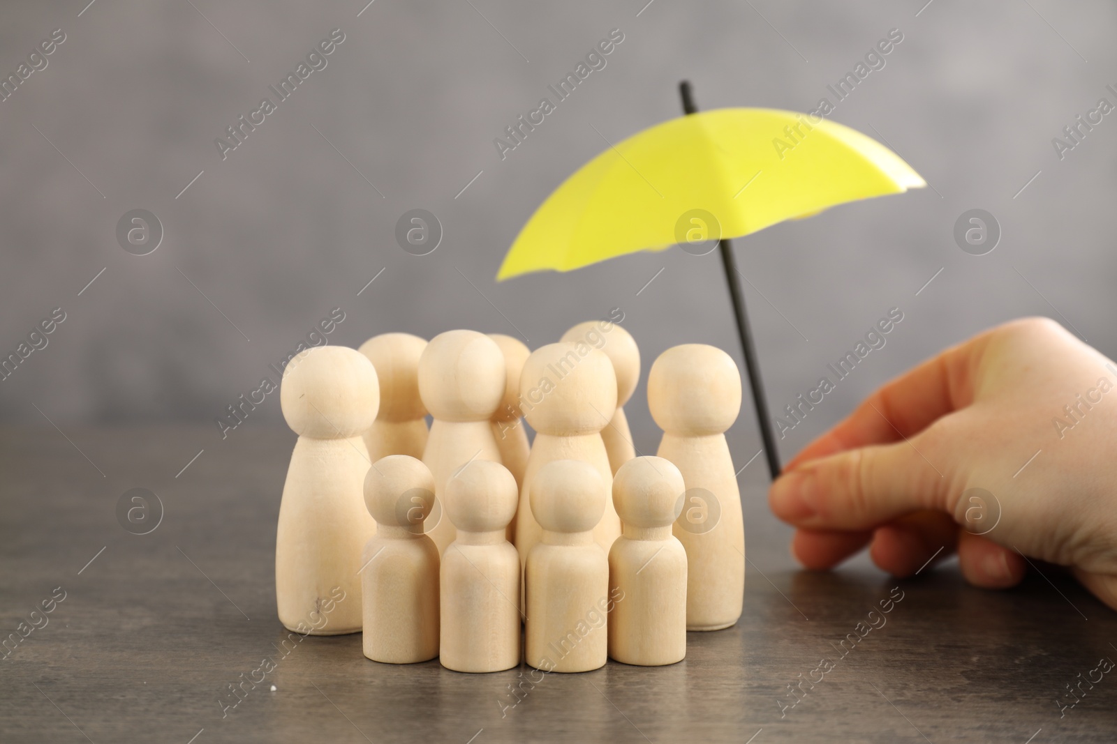 Photo of Woman holding umbrella over human figures at grey table, closeup. Insurance concept