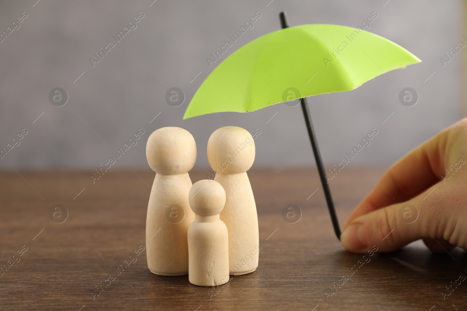 Photo of Woman holding umbrella over human figures at wooden table, closeup. Insurance concept