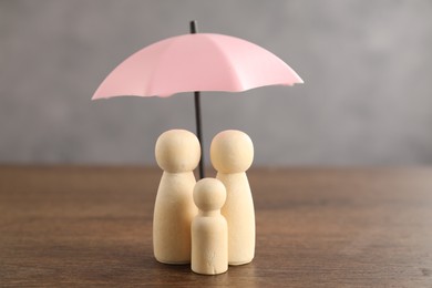 Photo of Human figures under umbrella on wooden table. Insurance concept