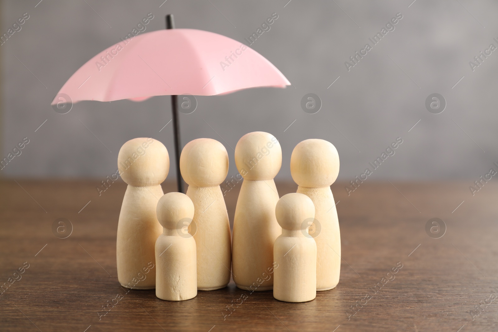 Photo of Human figures under umbrella on wooden table. Insurance concept