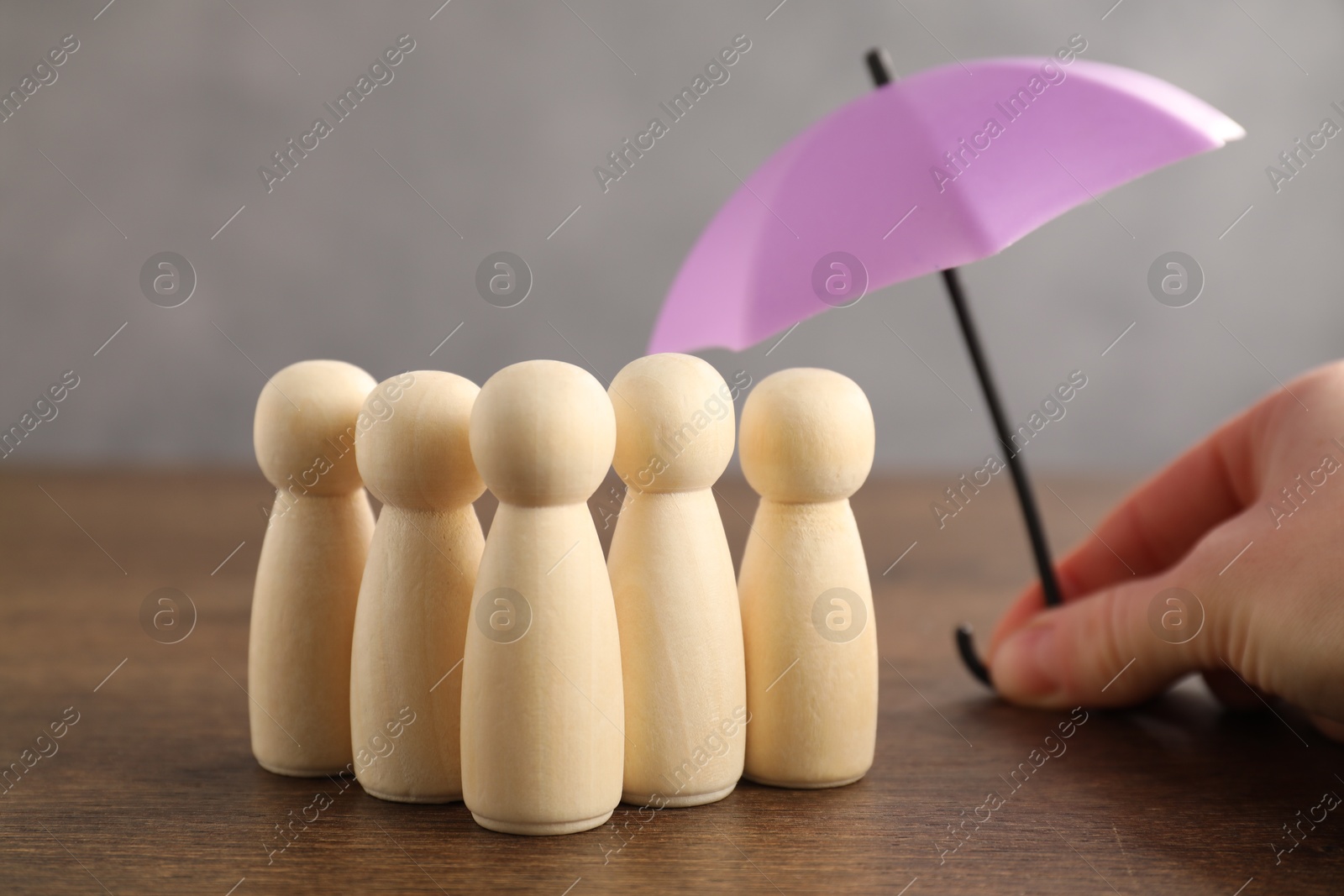 Photo of Woman holding umbrella over human figures at wooden table, closeup. Insurance concept