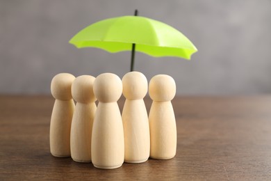 Photo of Human figures under umbrella on wooden table. Insurance concept