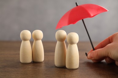 Photo of Woman holding umbrella over human figures at wooden table, closeup. Insurance concept