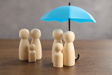 Photo of Human figures under umbrella and wooden ones on table. Insurance concept