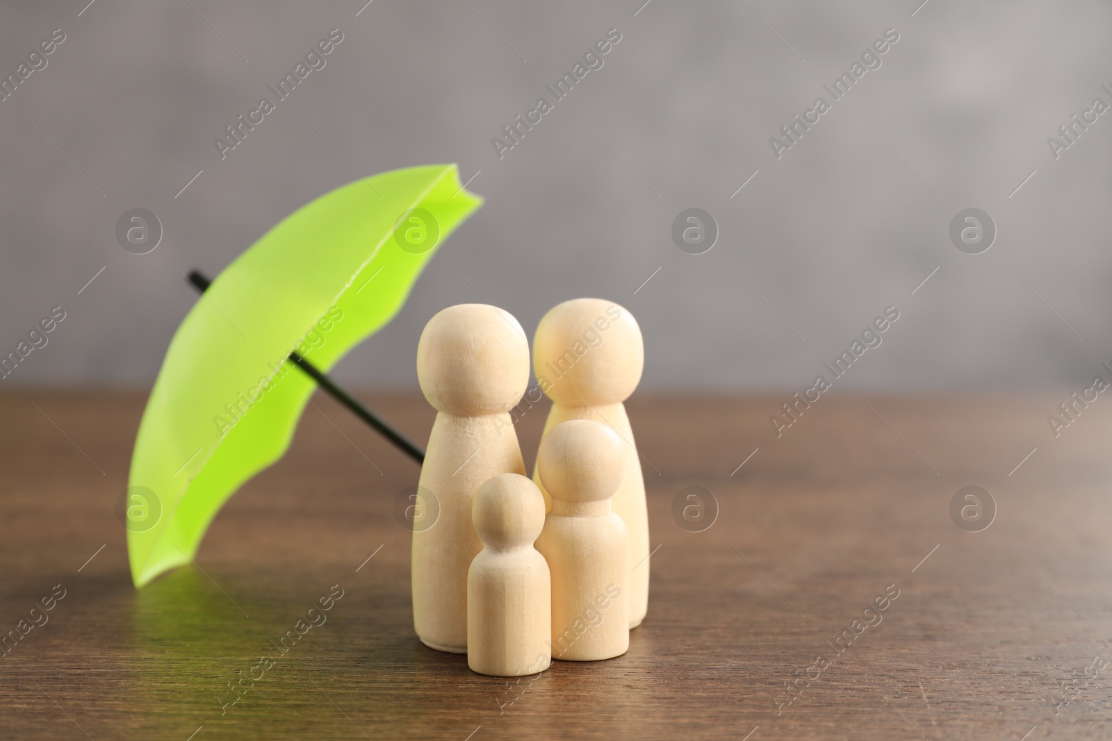 Photo of Human figures under umbrella on wooden table. Insurance concept