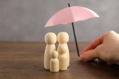 Photo of Woman holding umbrella over human figures at wooden table, closeup. Insurance concept