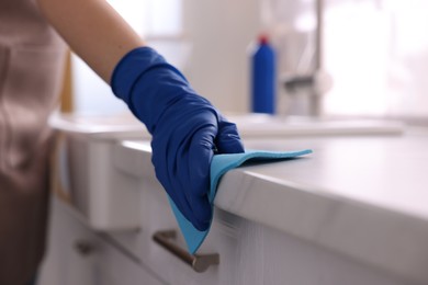 Photo of Woman wiping countertop with rag indoors, closeup