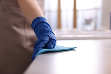 Photo of Woman wiping countertop with rag indoors, closeup