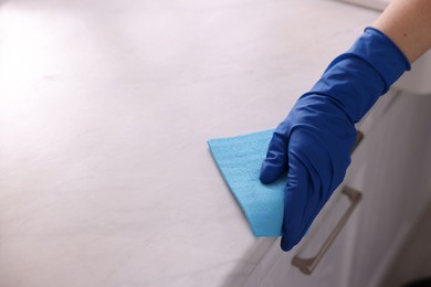 Photo of Woman wiping countertop with rag indoors, closeup. Space for text