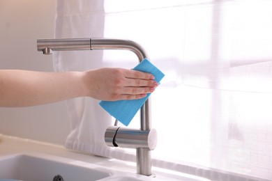 Photo of Woman wiping faucet of kitchen sink with rag indoors, closeup