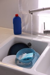 Photo of Dishes, blue sponge and foam under tap water in kitchen sink, closeup