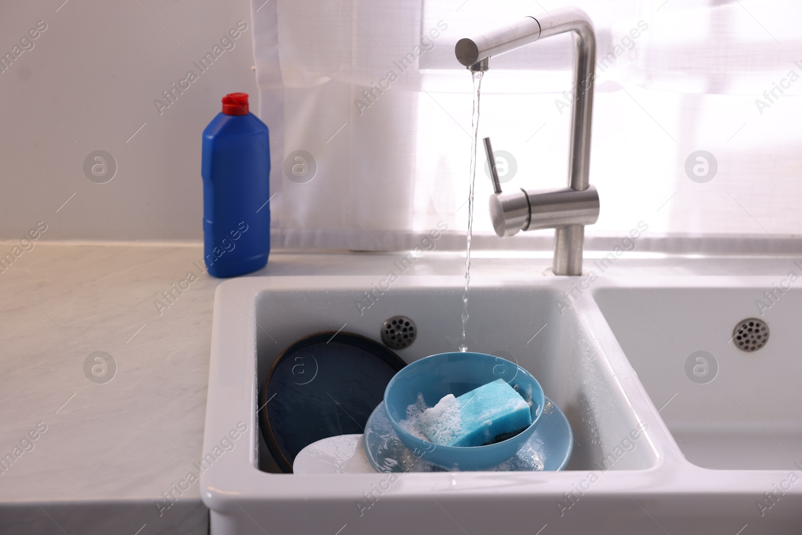 Photo of Dishes, blue sponge and foam in kitchen sink