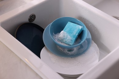 Photo of Dishes, blue sponge and foam in kitchen sink, closeup